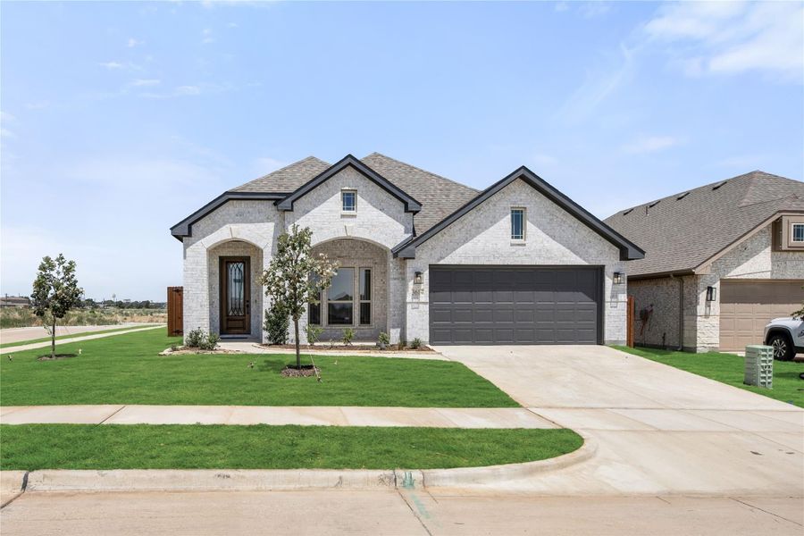 Single-story home with white brick exterior, arched entry, two-car garage, and green front lawn