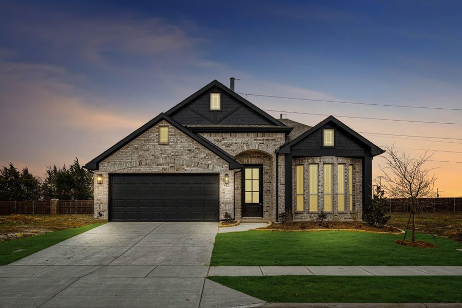 Single-story brick home with dark trim, two-car garage, arched entry, and front lawn at dusk