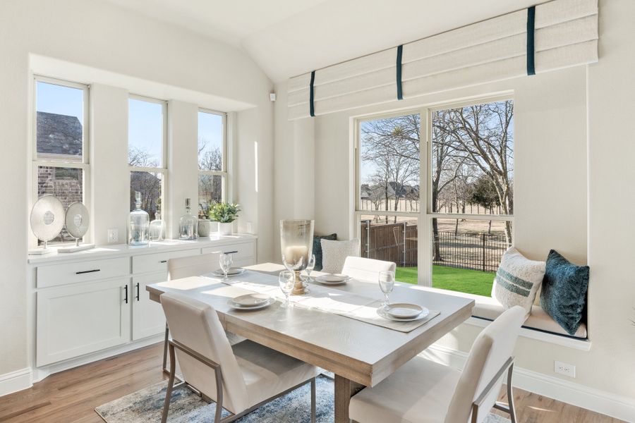 Bright dining area with wood table, white chairs, built-in window seat, and large windows overlooking backyard Bright dining area with wood table, white chairs, built-in window seat, and large windows overlooking backyard