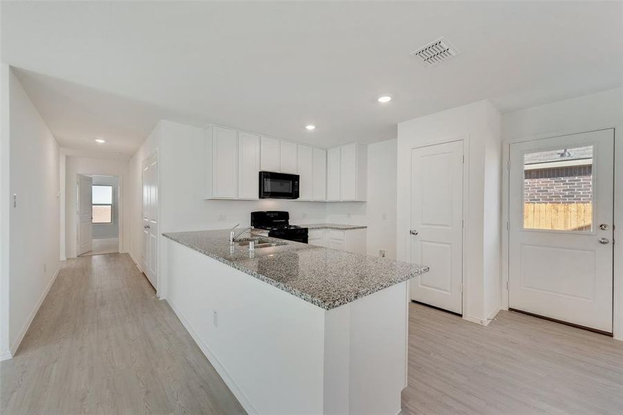 Kitchen featuring kitchen peninsula, light hardwood / wood-style flooring, white cabinetry, black appliances, and light stone countertops