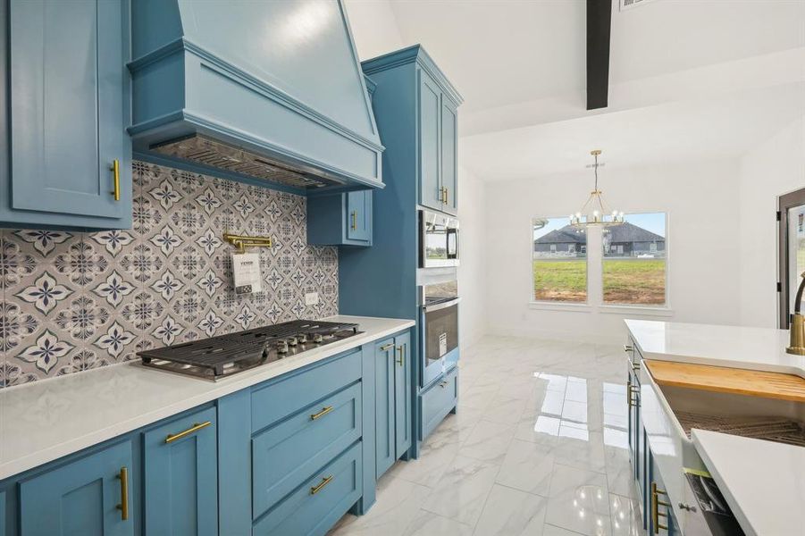 Kitchen featuring blue cabinetry, hanging light fixtures, premium range hood, a chandelier, and stainless steel gas stovetop