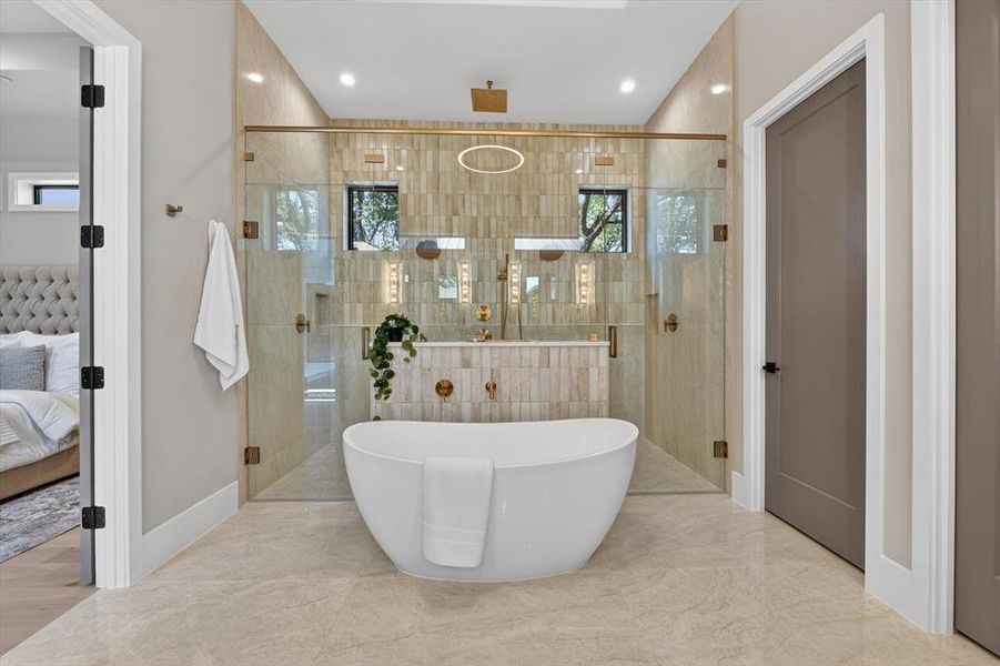 Freestanding soaking tub with gold-tone fixtures, surrounded by a glass-enclosed shower with vertical tile accents Freestanding soaking tub with gold-tone fixtures, surrounded by a glass-enclosed shower with vertical tile accents