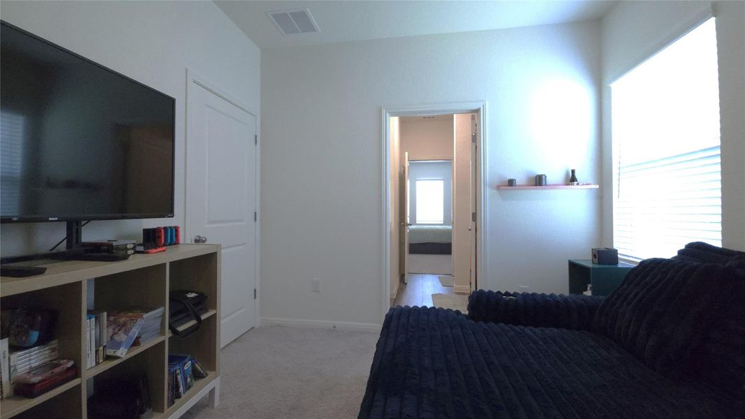 Carpeted room featuring a window with horizontal blinds, a built-in wall shelf, and a doorway opening to a hallway with wood-finish flooring
