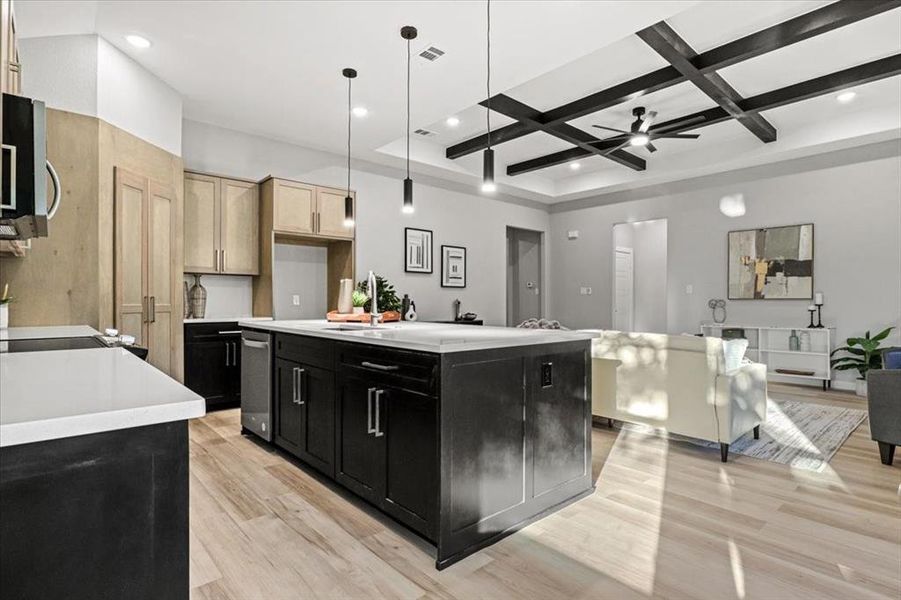 Kitchen featuring ceiling fan, an island with sink, decorative light fixtures, and coffered ceiling