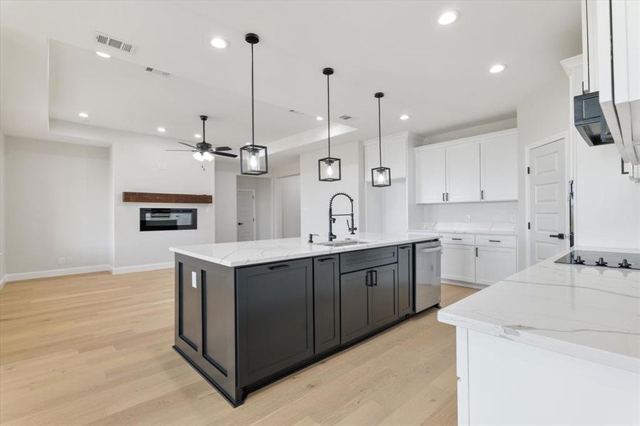 Kitchen with a kitchen island with sink, white cabinets, a sink, and hanging light fixtures