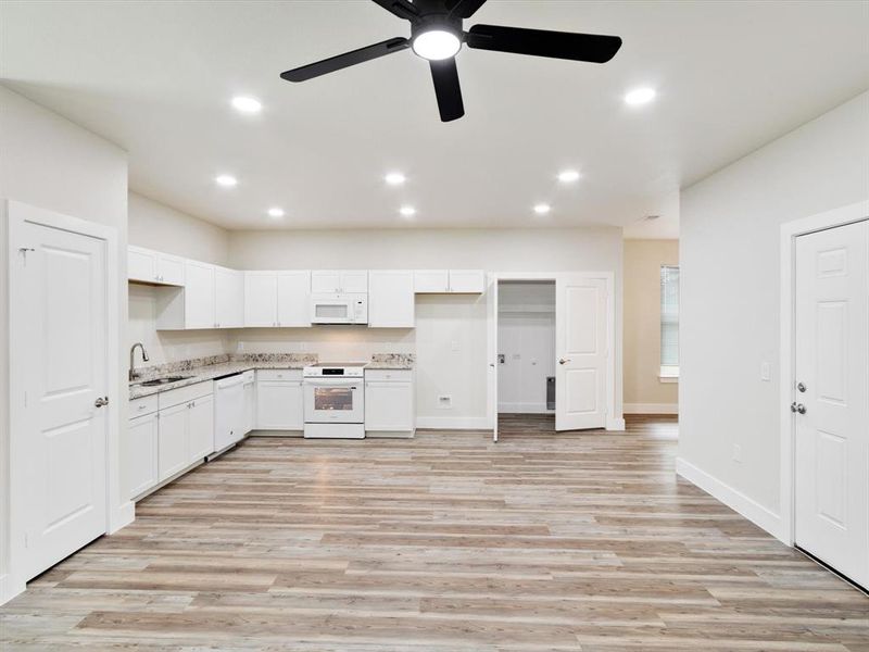 Open-concept living area featuring a kitchen with white cabinetry, light-toned countertops, and built-in appliances Open-concept living area featuring a kitchen with white cabinetry, light-toned countertops, and built-in appliances