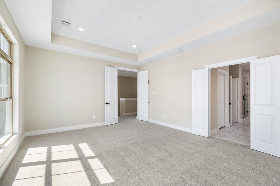 The generously-sized primary bedroom is filled with natural light, featuring plush carpeting and large windows that create a welcoming atmosphere. French doors open to both the bedroom and the en-suite bathroom, offering a seamless flow. Take a closer look at the modern finishes in the bathroom and the thoughtful design that enhances this serene space.