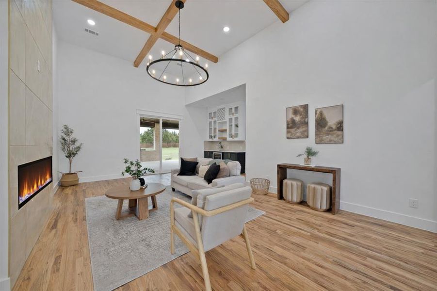 The spacious living area features hardwood floors, a modern fireplace, vaulted ceilings with exposed beams, and a view of the outdoor patio and lawn