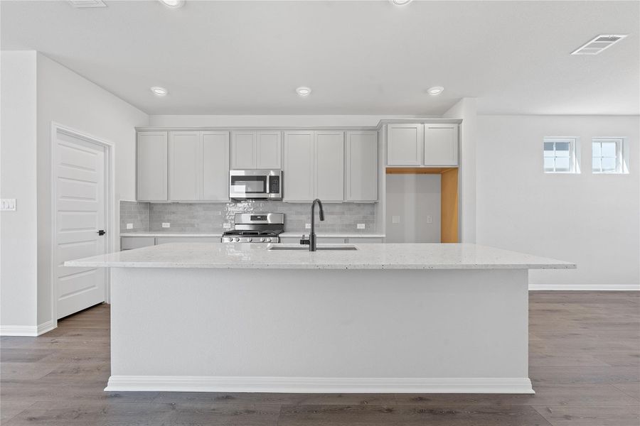 Kitchen with an island with sink, tasteful backsplash, appliances with stainless steel finishes, light stone countertops, and wood finished floors