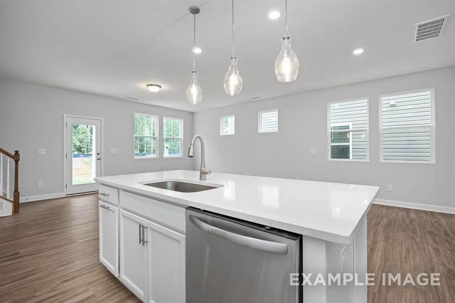 Kitchen featuring decorative light fixtures, dishwasher, sink, white cabinets, and a kitchen island with sink