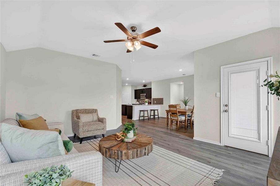 Open concept living area featuring wood-finish flooring, vaulted ceilings, and a ceiling fan with integrated lighting Open concept living area featuring wood-finish flooring, vaulted ceilings, and a ceiling fan with integrated lighting