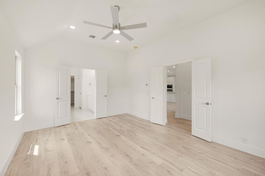 Empty bedroom with light wood floors, ceiling fan, and doors leading to closet and bathroom