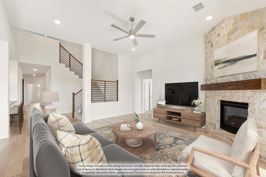 Open living room with high ceilings, stone fireplace, ceiling fan, and staircase visible in background Open living room with high ceilings, stone fireplace, ceiling fan, and staircase visible in background