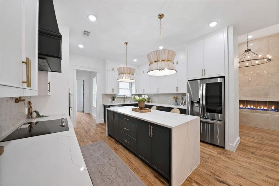 The kitchen features a center island with a white countertop and dark cabinetry, along with white upper cabinets and gold hardware