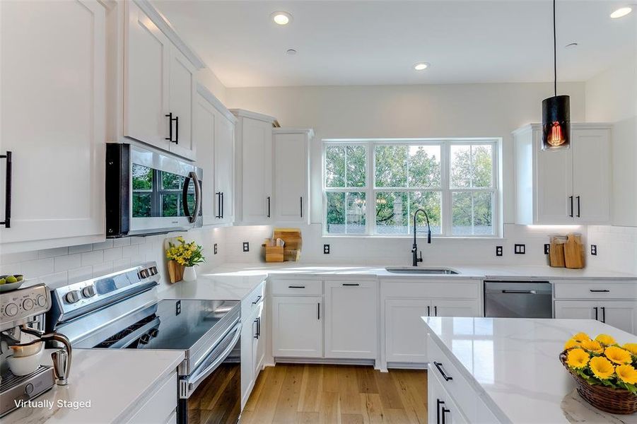 Kitchen with appliances with stainless steel finishes, light wood-type flooring, a sink, and white cabinetry