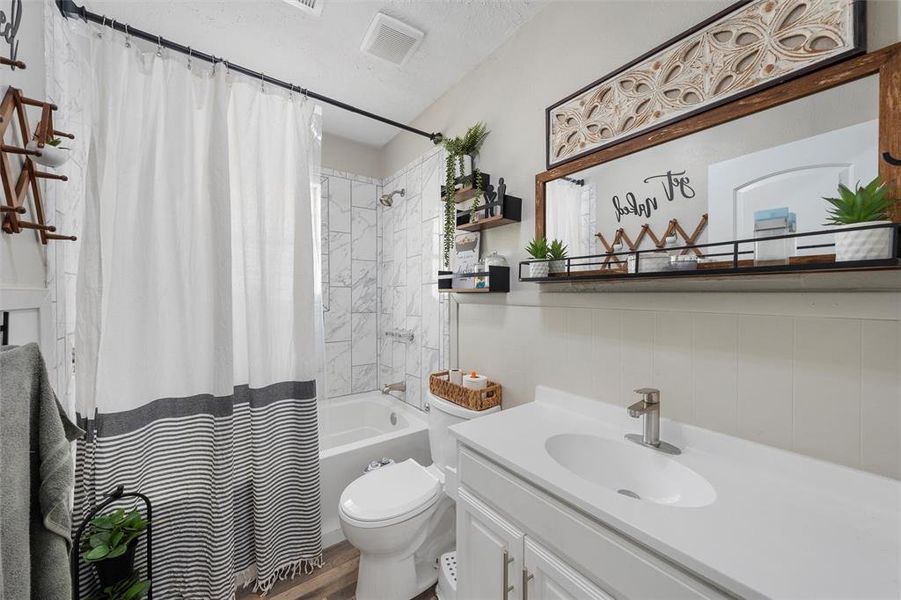 Full bathroom featuring vanity, toilet, shower / tub combo with curtain, and wood finished floors Full bathroom featuring vanity, toilet, shower / tub combo with curtain, and wood finished floors
