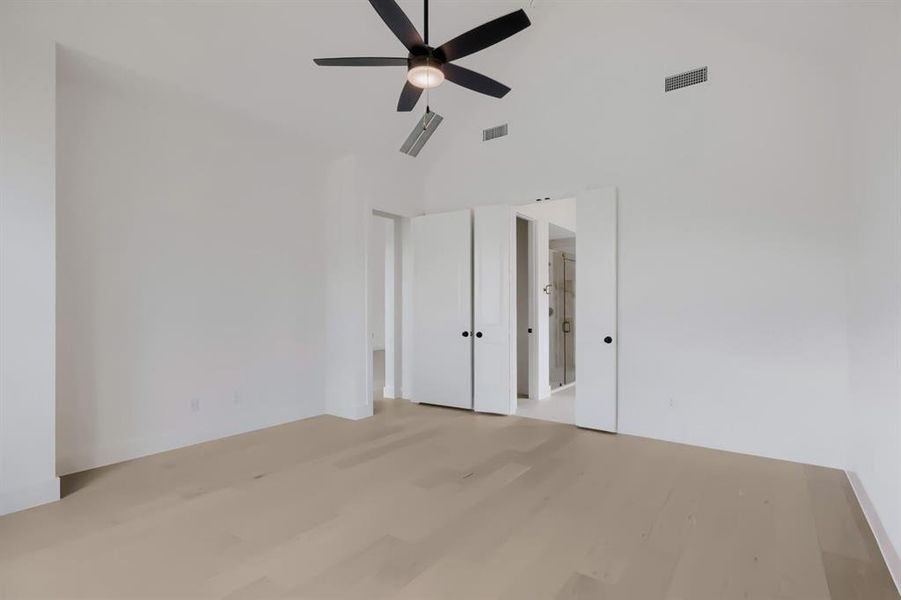 Spacious room featuring vaulted ceilings, a black ceiling fan with integrated lighting, light wood-finish flooring, and white bifold doors revealing an en-suite bathroom with a glass-enclosed shower Spacious room featuring vaulted ceilings, a black ceiling fan with integrated lighting, light wood-finish flooring, and white bifold doors revealing an en-suite bathroom with a glass-enclosed shower