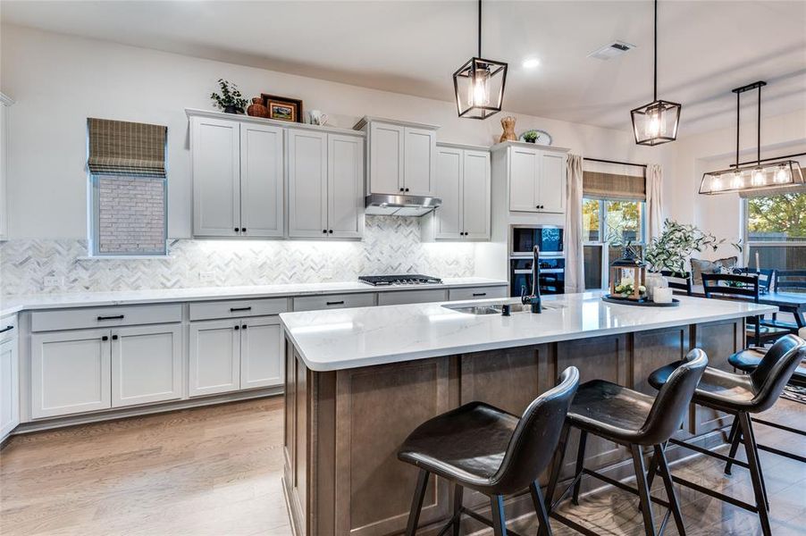 Kitchen featuring light stone countertops, hanging light fixtures, decorative backsplash, a kitchen bar, and recessed lighting