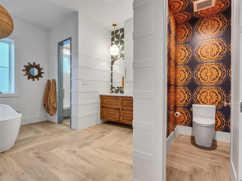 A stunning corner view of the primary bath showcases serene soaking tub, sleek glass-enclosed shower, and dual vanities under soft, flattering light. The private toilet area with custom wallpaper adds designer flair. From herringbone tile floors to refined coastal finishes, every detail invites relaxation — your own private retreat after a sun-soaked day at the beach or a long day’s work. A stunning corner view of the primary bath showcases serene soaking tub, sleek glass-enclosed shower, and dual vanities under soft, flattering light. The private toilet area with custom wallpaper adds designer flair. From herringbone tile floors to refined coastal finishes, every detail invites relaxation — your own private retreat after a sun-soaked day at the beach or a long day’s work.