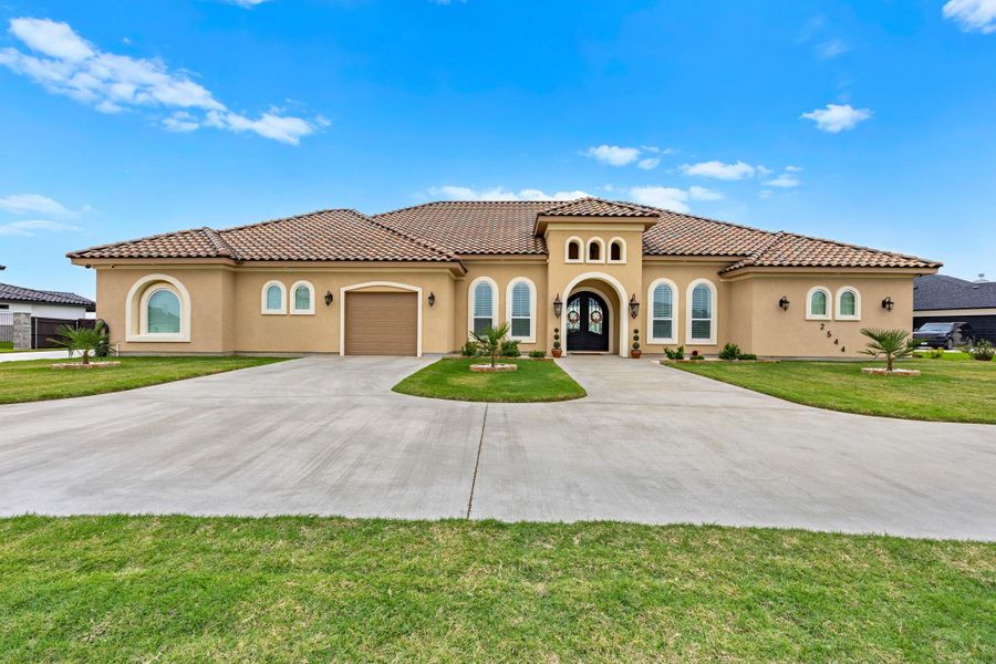 A grand Mediterranean-inspired residence presents a spacious driveway and manicured lawn under a wide-open sky. A grand Mediterranean-inspired residence presents a spacious driveway and manicured lawn under a wide-open sky.