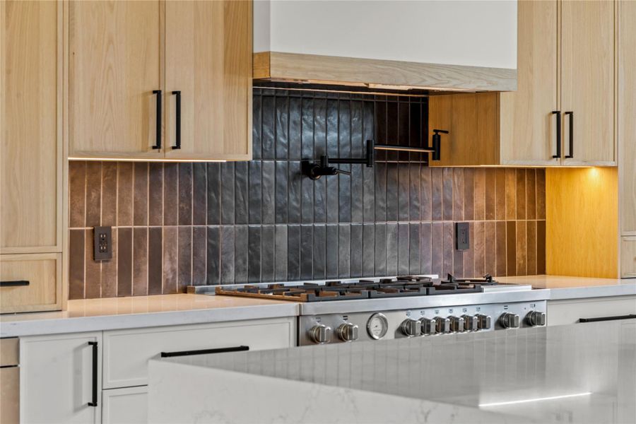 Kitchen view of decorative backsplash, pot filler, and light brown cabinetry