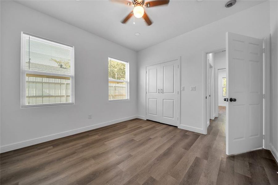 Unfurnished bedroom with multiple windows, a closet, dark wood-style flooring, and ceiling fan