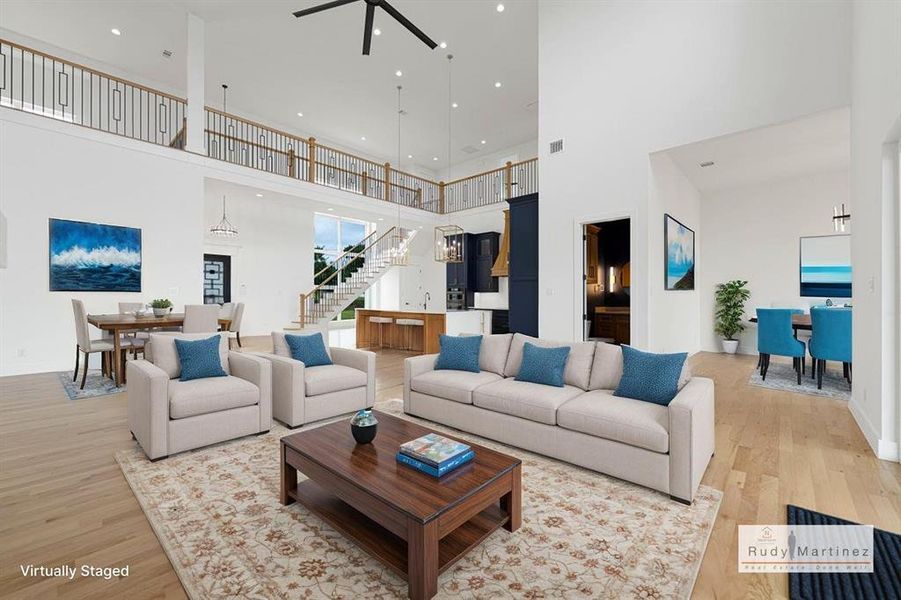 Living room with light wood-style flooring, a ceiling fan, a high ceiling, and a chandelier