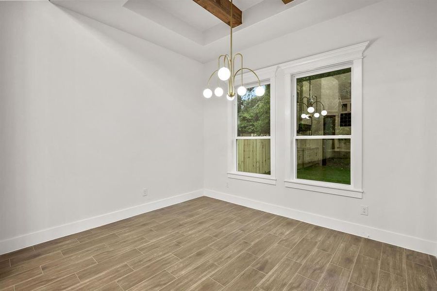 Open room featuring wood-finish flooring, a modern chandelier, and a tray ceiling with exposed wood beams