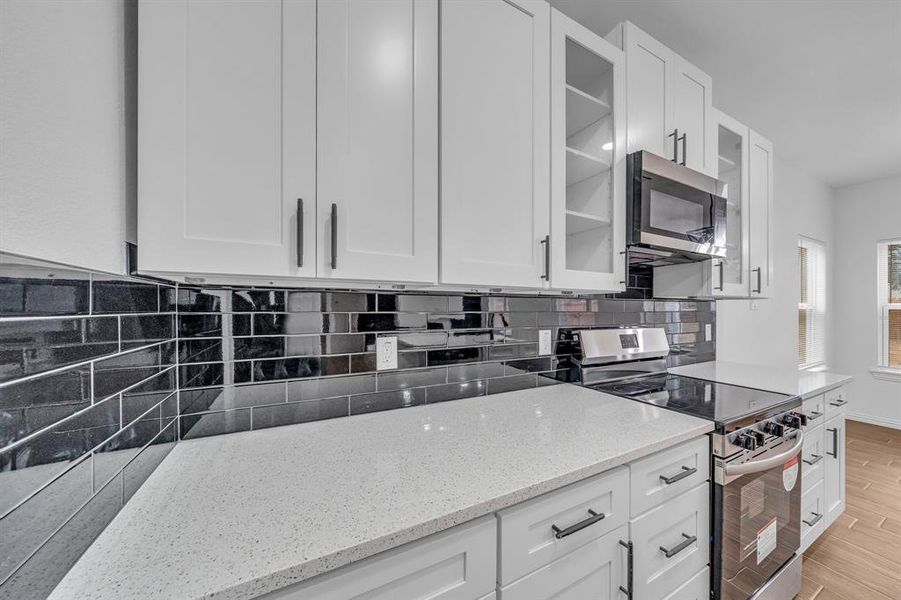 Kitchen with light hardwood / wood-style flooring, appliances with stainless steel finishes, light stone counters, white cabinets, and decorative backsplash