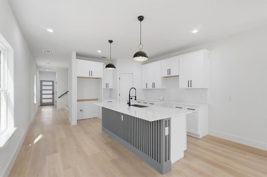 Kitchen featuring white cabinets, a kitchen island with sink, light wood finished floors, a kitchen bar, and decorative light fixtures