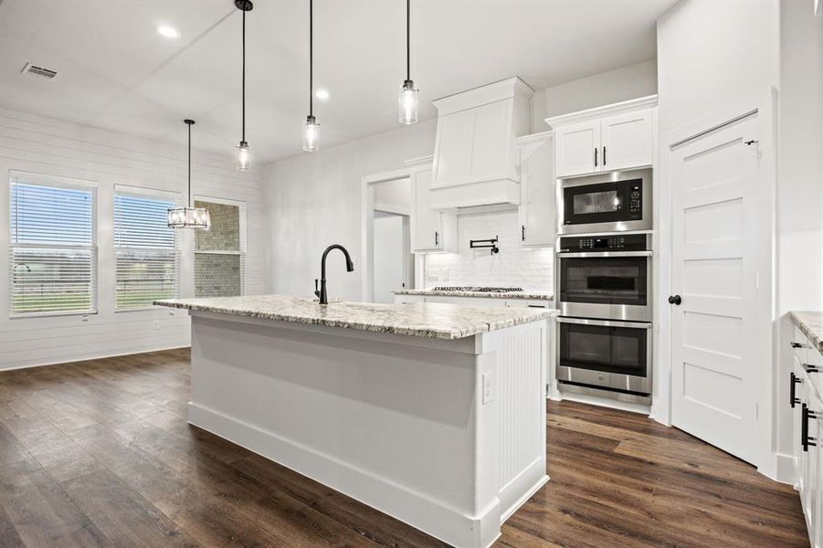 Kitchen with a center island with sink, white cabinets, hanging light fixtures, built in microwave, and stainless steel double oven