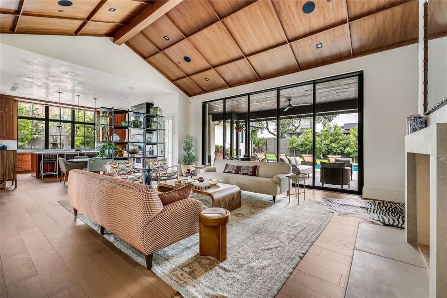 A spacious, naturally illuminated great room featuring a grand fireplace, exposed wooden beam ceilings, and hardwood floors.