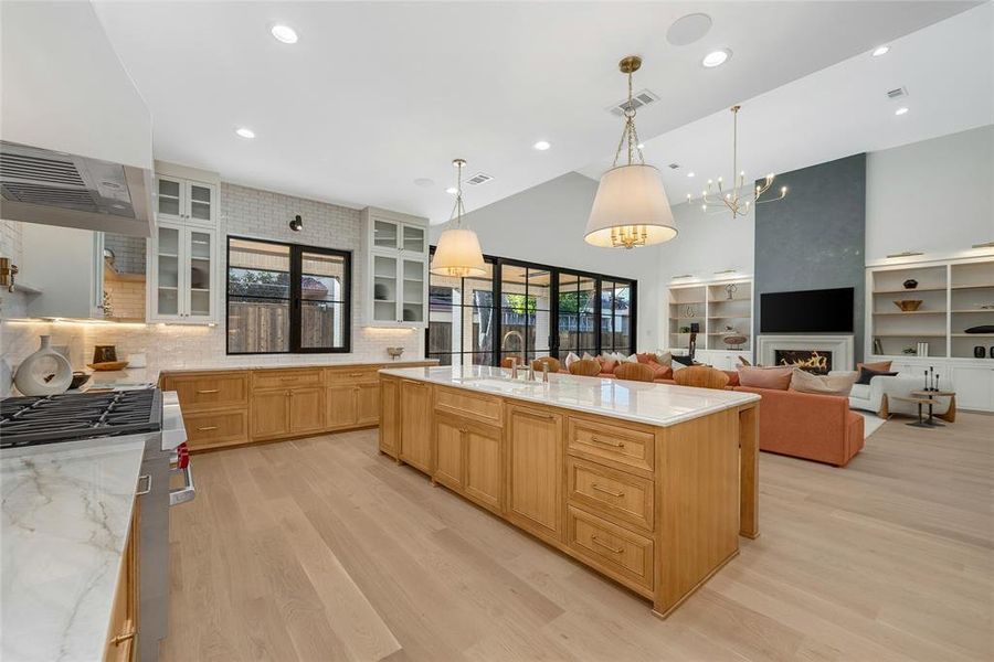 Open-concept kitchen and living area featuring light wood-finish flooring, a large kitchen island with a white countertop, and light wood cabinetry