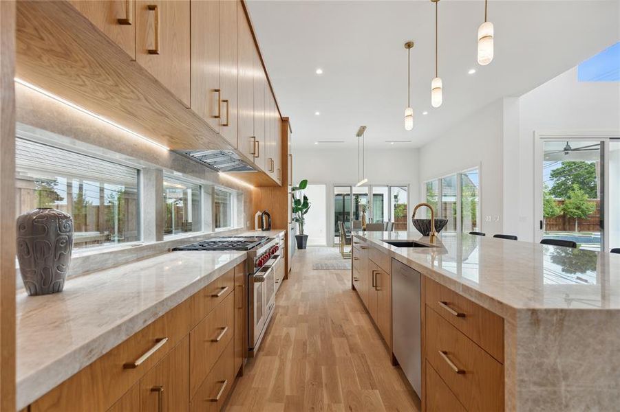 Kitchen with decorative light fixtures, appliances with stainless steel finishes, light hardwood / wood-style floors, a large island, and sink