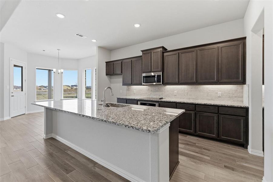 Kitchen featuring light stone counters, a center island with sink, dark wood finish cabinets, and light wood-type flooring