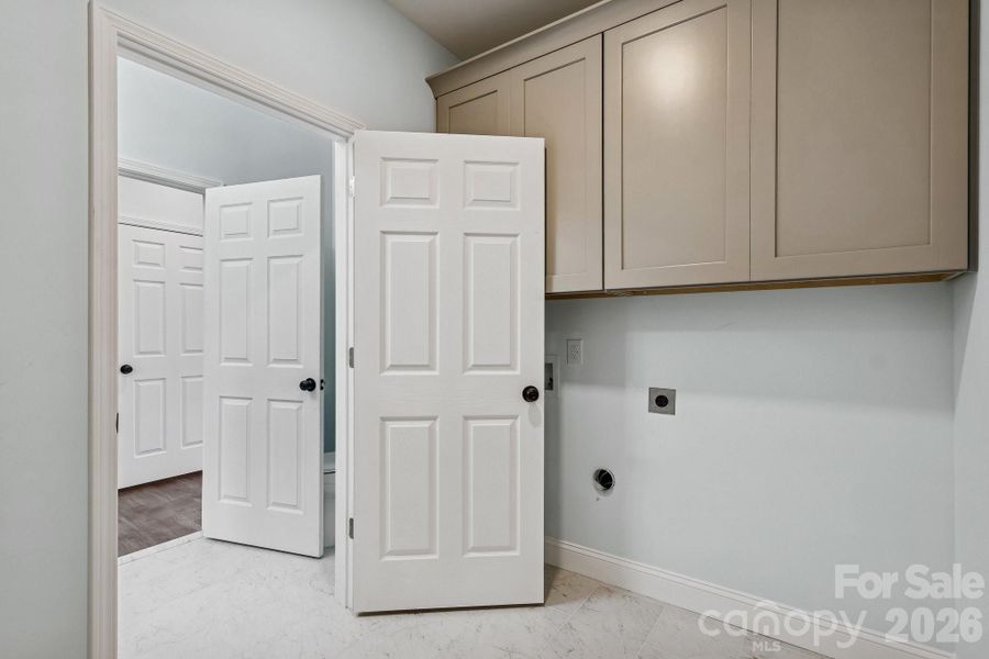 first floor laundry room with tile flooring and large cabinetry for storage
