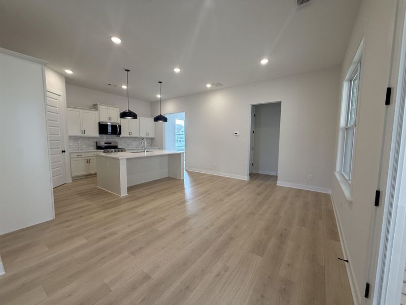 Kitchen with white cabinetry, a center island with sink, decorative light fixtures, stainless steel appliances, and tasteful backsplash