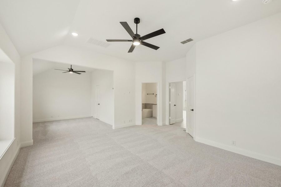 Large empty bedroom with gray carpet, two ceiling fans, and an open ensuite bathroom doorway