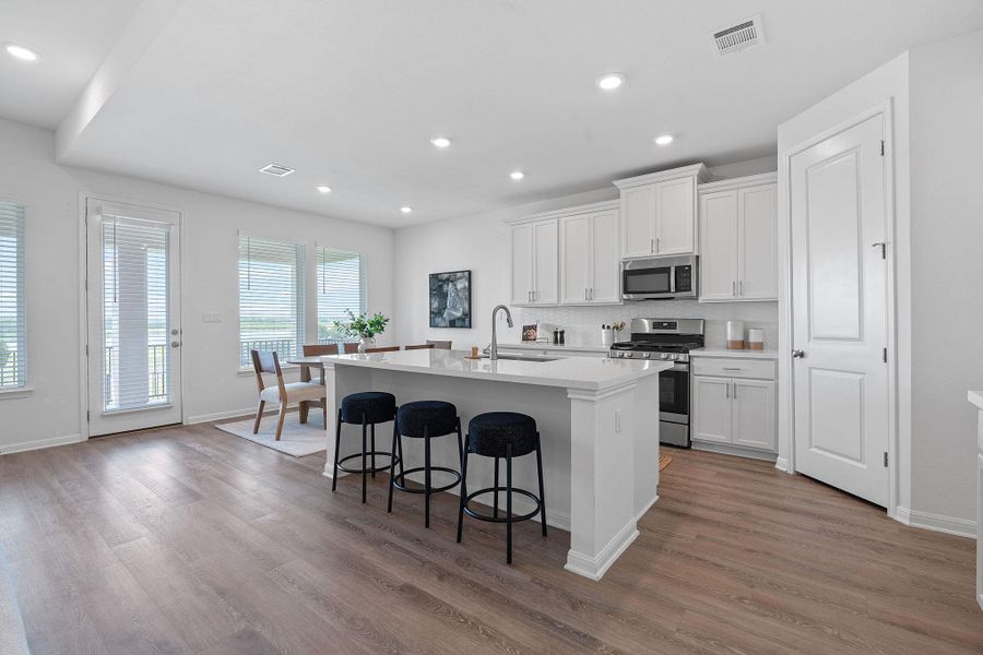 Kitchen with stainless steel appliances, a sink, a center island with sink, wood finished floors, and recessed lighting