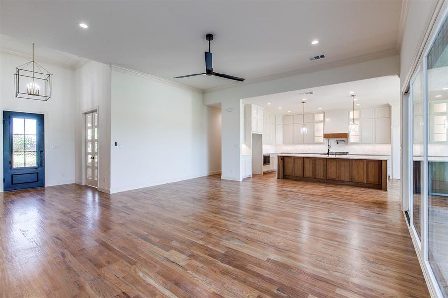 Unfurnished living room featuring ceiling fan with notable chandelier, light hardwood / wood-style floors, and crown molding