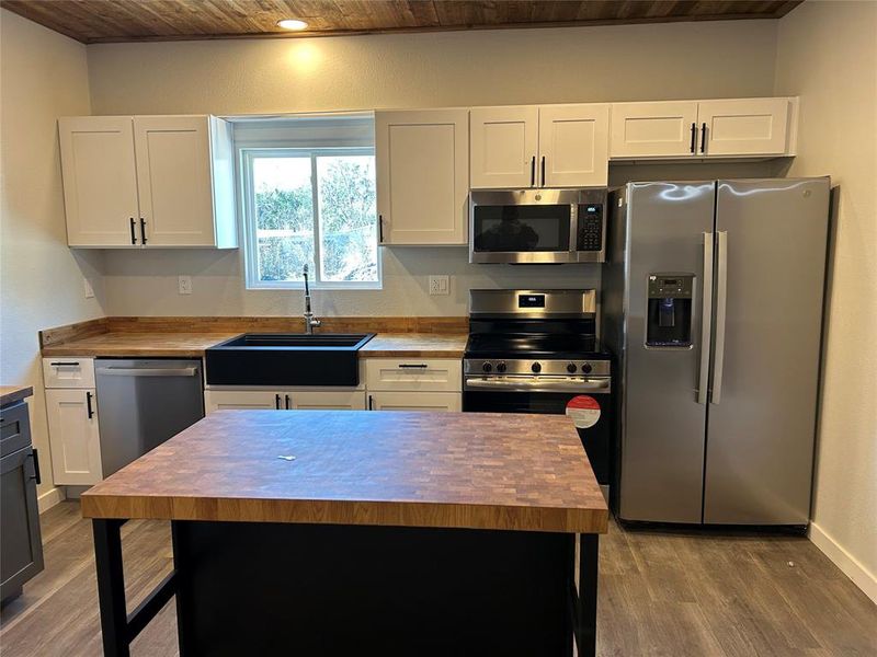 Kitchen with stainless steel appliances, wooden ceiling, white cabinets, dark wood-type flooring, and butcher block counters Kitchen with stainless steel appliances, wooden ceiling, white cabinets, dark wood-type flooring, and butcher block counters