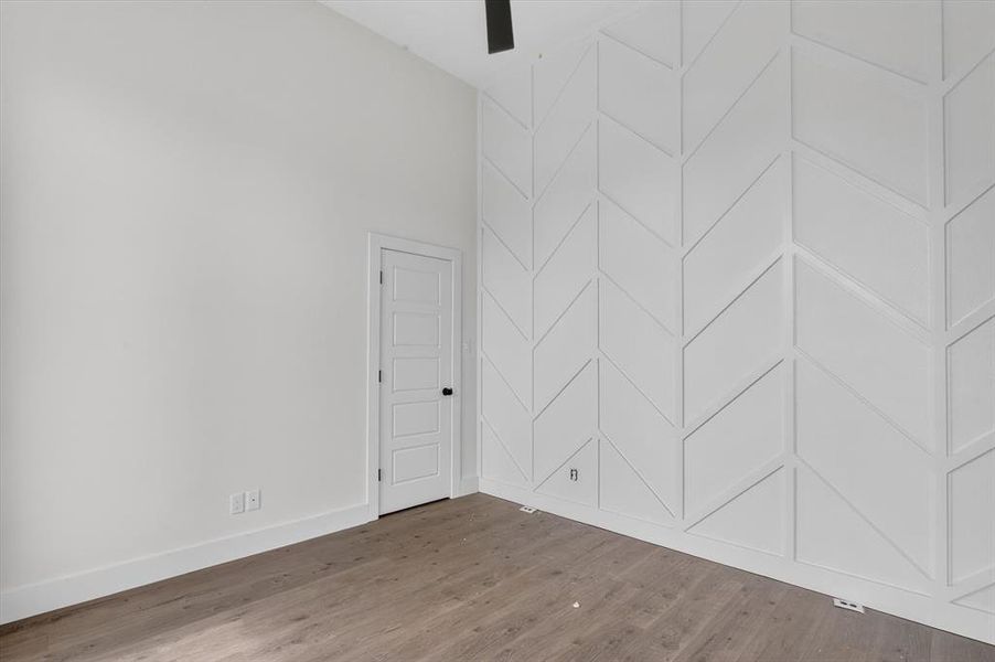 Vaulted ceiling room featuring a decorative accent wall with a geometric pattern, wood-finish flooring, and a paneled interior door with black hardware Vaulted ceiling room featuring a decorative accent wall with a geometric pattern, wood-finish flooring, and a paneled interior door with black hardware