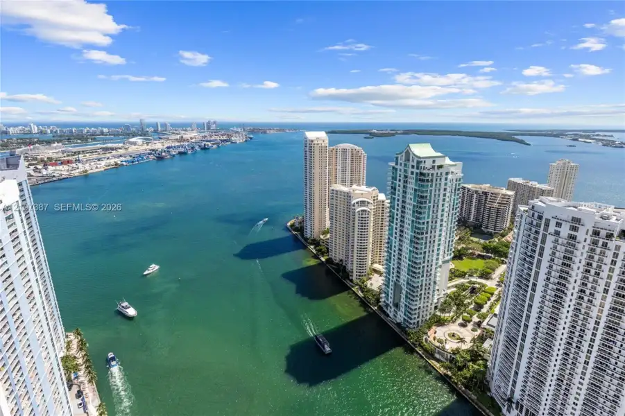 Aerial perspective of waterfront urban skyline featuring high-rise buildings, deep-water channel, maritime traffic, and proximity to expansive harbor scenery