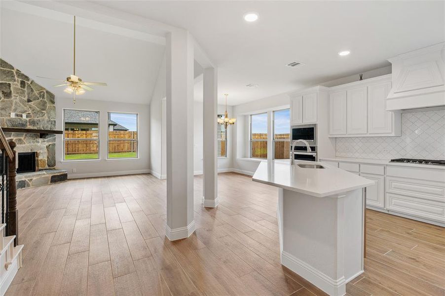 Kitchen with backsplash, open floor plan, white cabinets, light wood-style floors, and a fireplace