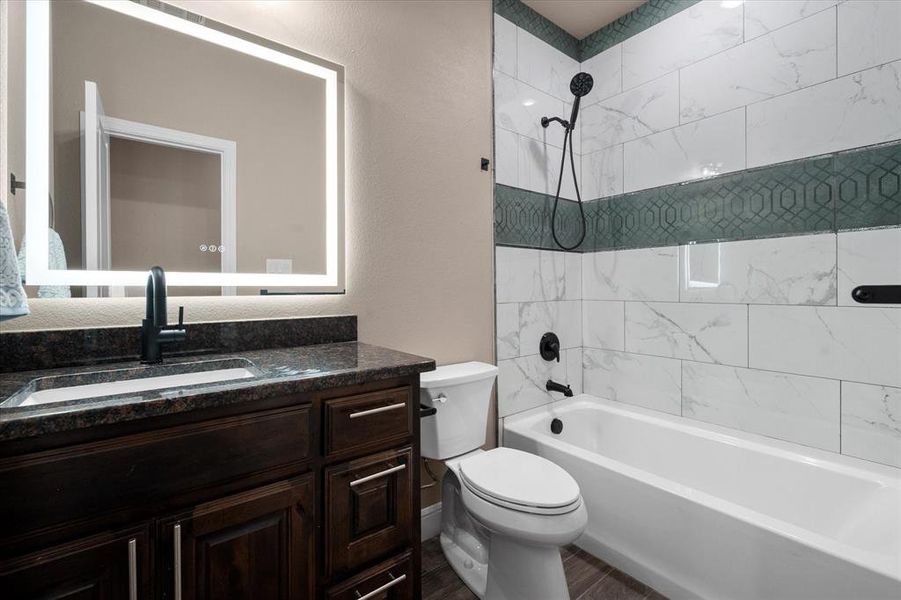 Bathroom featuring a dark wood vanity with a granite countertop, an illuminated mirror, and a white bathtub