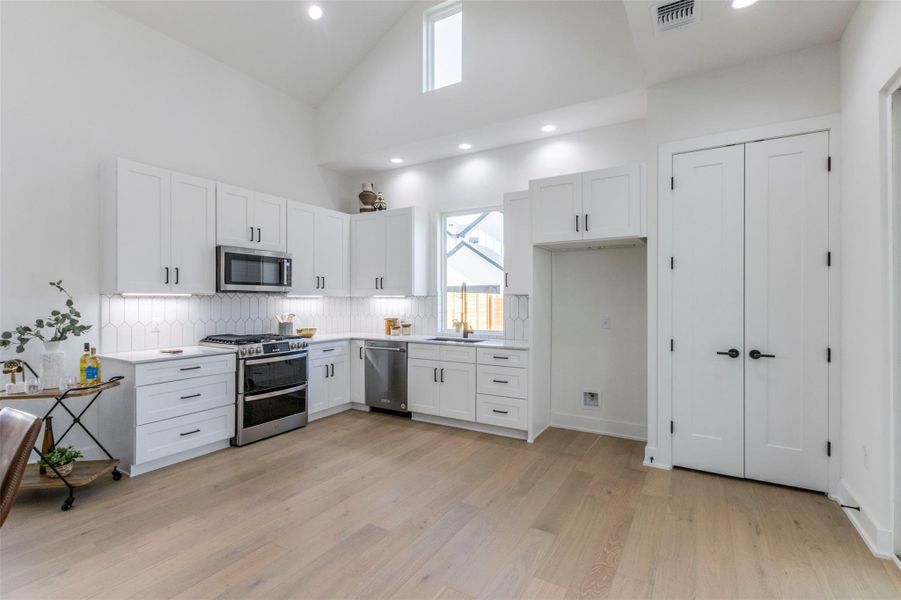 Kitchen featuring stainless steel appliances, white cabinetry, high vaulted ceiling, recessed lighting, and light wood-style floors