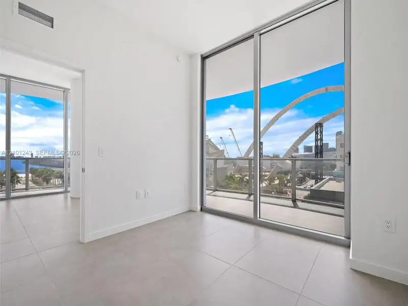 Floor-to-ceiling sliding glass doors, private balcony with metal railing, large-format tile flooring, and neutral wall finishes Floor-to-ceiling sliding glass doors, private balcony with metal railing, large-format tile flooring, and neutral wall finishes