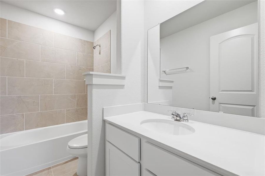Bathroom featuring a tub/shower combination with large format tile surround, a built-in vanity with an integrated sink, a rectangular mirror, and a contemporary toilet Bathroom featuring a tub/shower combination with large format tile surround, a built-in vanity with an integrated sink, a rectangular mirror, and a contemporary toilet
