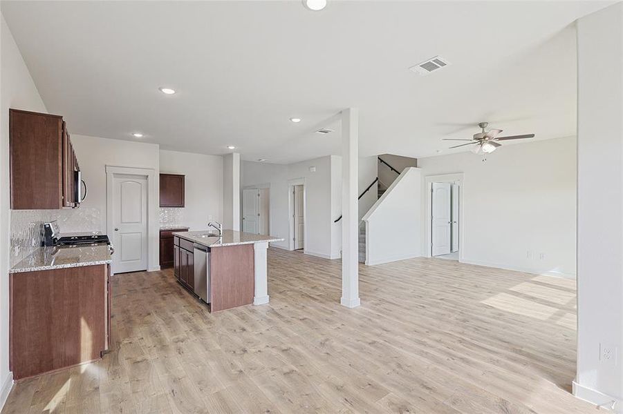 Kitchen with light stone countertops, stainless steel appliances, tasteful backsplash, an island with sink, and light wood-type flooring