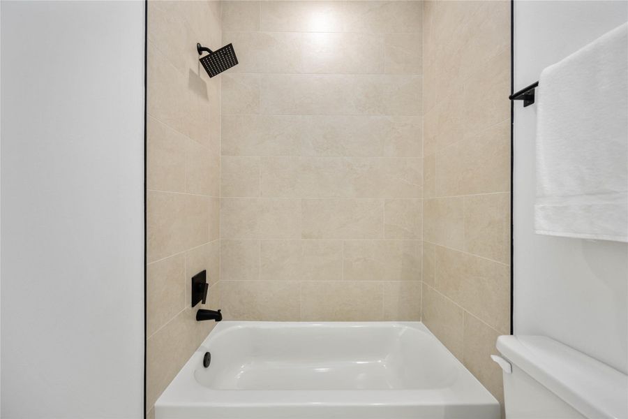This modern tub-shower combo features large-format neutral tile walls, matte black fixtures, and clean minimalist lines, creating a fresh and contemporary spa-like feel.